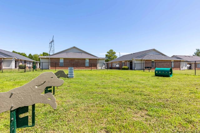 Dog park area with green tunnel, agility equipment, and benches within a fenced-in yard.