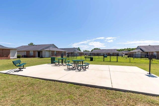Picnic tables and benches on concrete patio with apartment buildings in background.