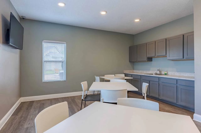 Community room with tables, chairs, and a kitchenette.
