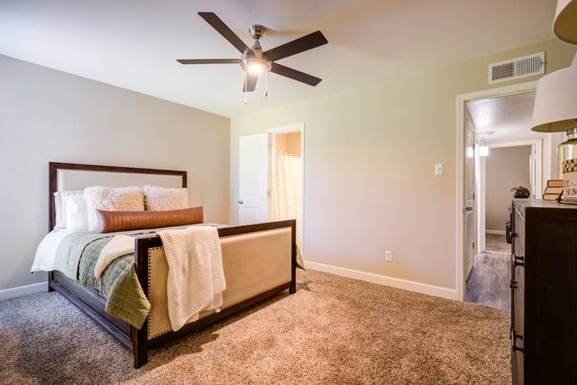 Bedroom with a large bed, ceiling fan, and an open doorway leading to a hallway.