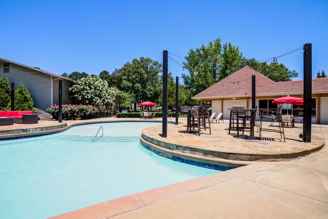 Sparkling blue swimming pool with lounge chairs and outdoor dining tables under a clear blue sky.