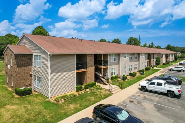 Exterior of apartment building with parking lot and green lawn.