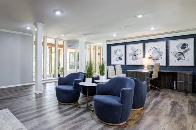 Lobby seating area with blue chairs, small tables, and abstract art on the wall.