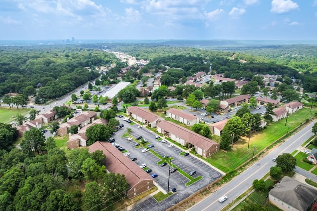 Aerial view of an apartment complex surrounded by trees, with buildings and parking lots visible.