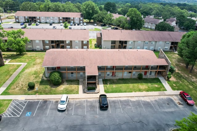 Aerial view of apartment buildings with parking lot and green spaces.
