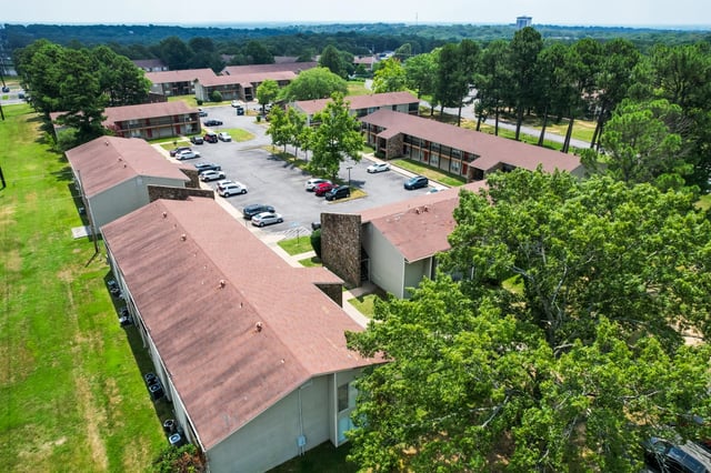 Aerial view of apartment buildings with parking lots and surrounding trees.