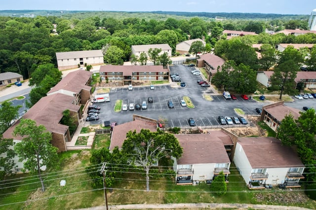 Aerial view of apartment buildings with parking lot and surrounding trees.