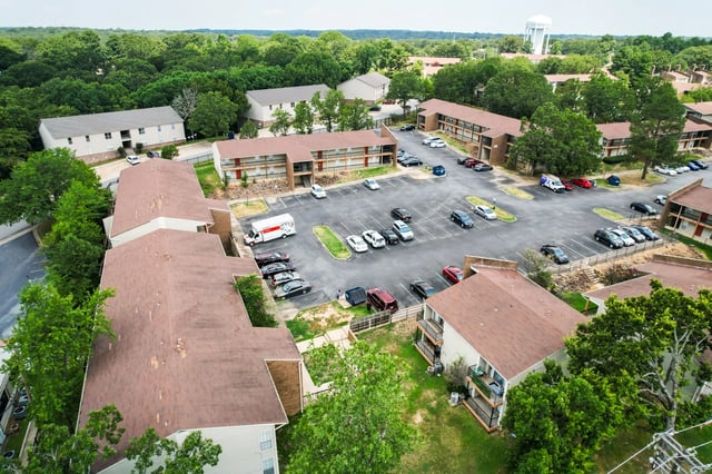 Aerial view of apartment buildings with parking lot and trees.
