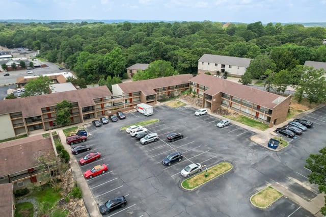 Aerial view of apartment buildings with parking lots and surrounding trees.