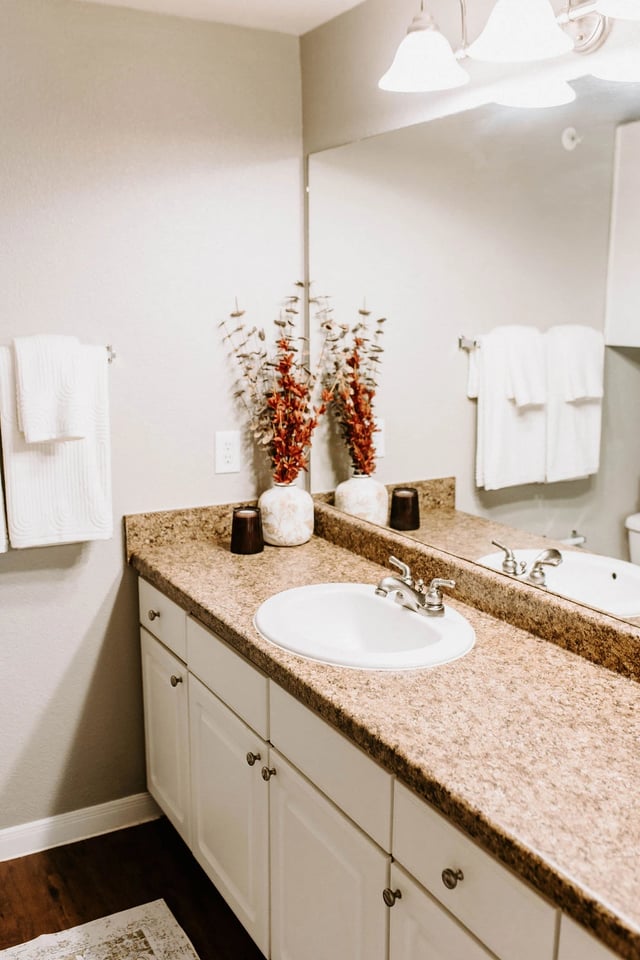 Bathroom vanity with a white sink, granite countertop, and decorative vases.