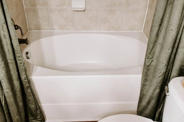 White bathtub with a green shower curtain.