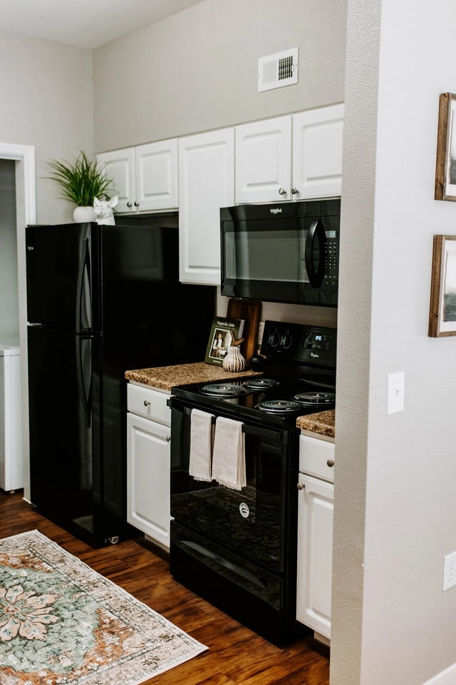 Kitchen with black refrigerator, oven, and microwave, plus white cabinets.