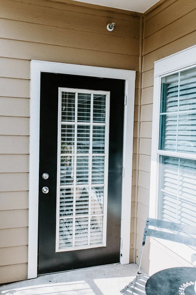 Exterior view of a dark front door with glass panes and blinds, next to a window.