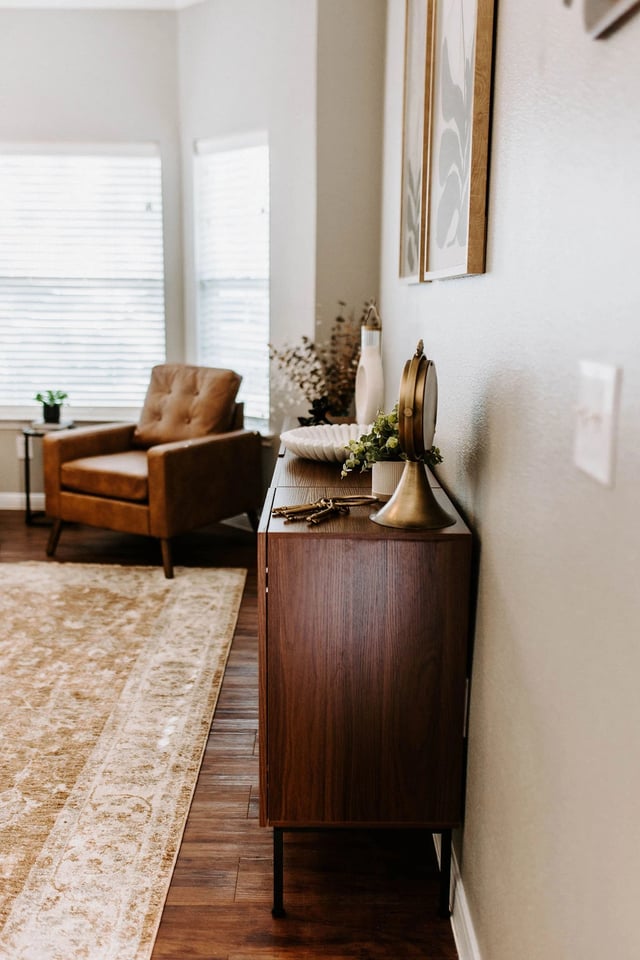 A stylish living room with a leather armchair, a dark wood cabinet, and a decorative rug.