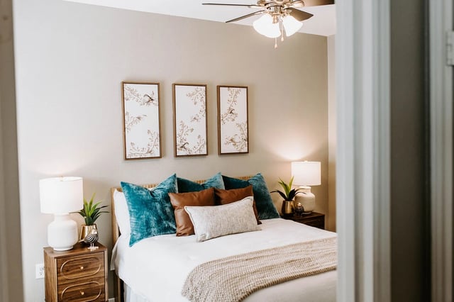 Bedroom with a queen-size bed, teal and brown pillows, and a ceiling fan.