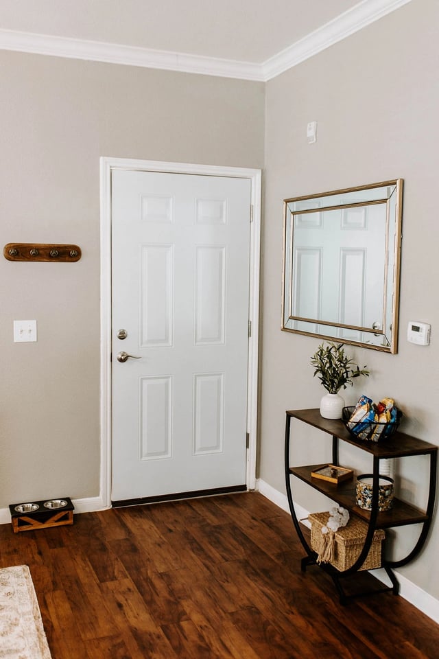 Entryway with white door, coat rack, mirror, and console table with decor.