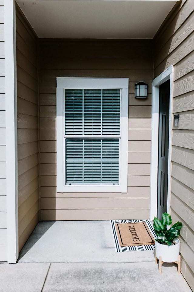 Exterior of an apartment building showing a front door, window, and welcome mat.