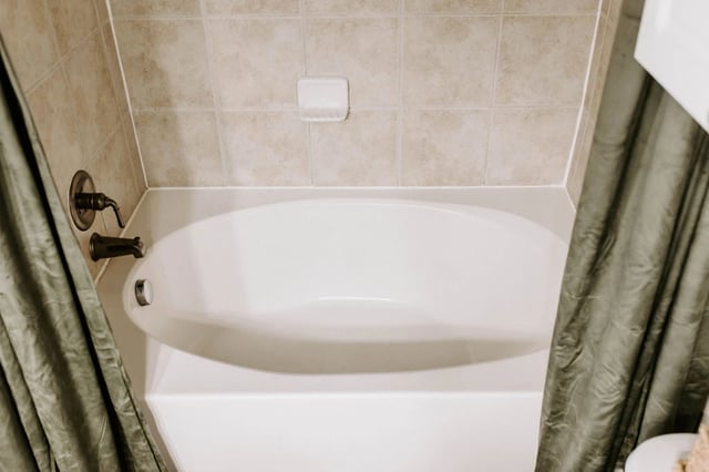 White bathtub with bronze fixtures and a green shower curtain.