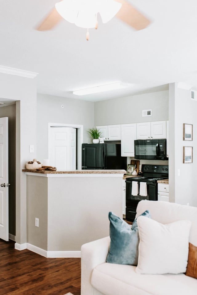 Modern kitchen with black appliances and white cabinets. A white sofa with blue pillows is in the foreground.