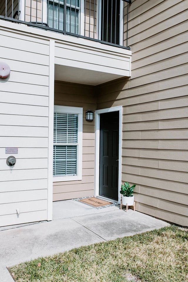 Exterior view of apartment building entrance with a black door and welcome mat.