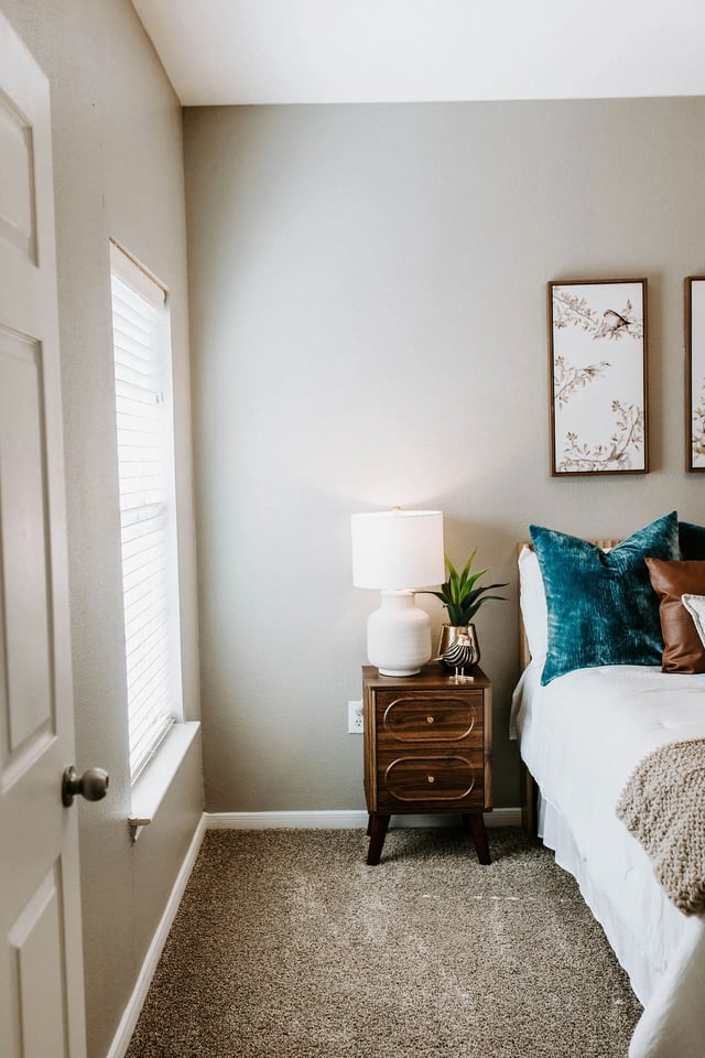 Bedroom with a white bed, teal and brown accent pillows, and a nightstand with a lamp.