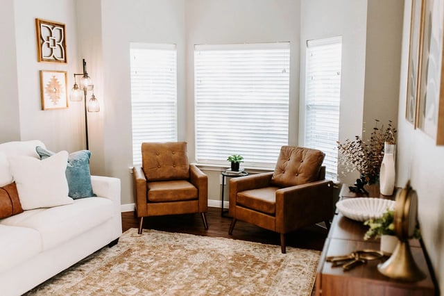 Living room with a white sofa, two brown accent chairs, and a large rug.