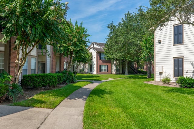 Exterior view of apartment buildings with lush green lawns and trees.