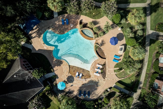 Aerial view of an outdoor swimming pool and spa with lounge chairs and umbrellas.
