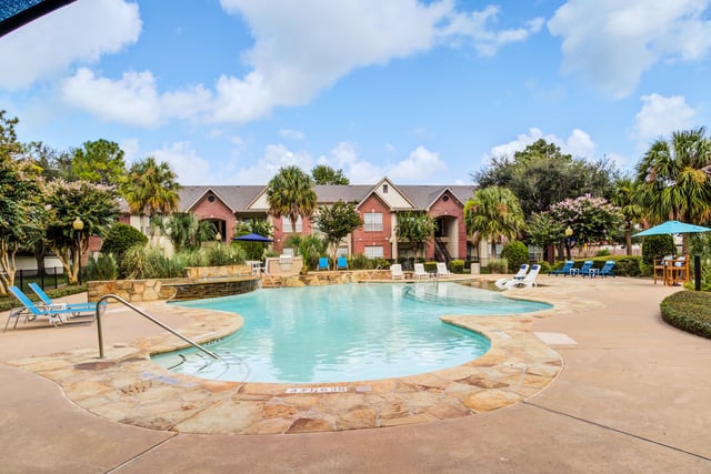 Resort-style swimming pool with lounge chairs and palm trees, overlooking apartment buildings.