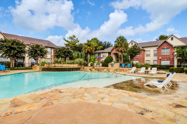 Resort-style swimming pool with lounge chairs and buildings in the background.
