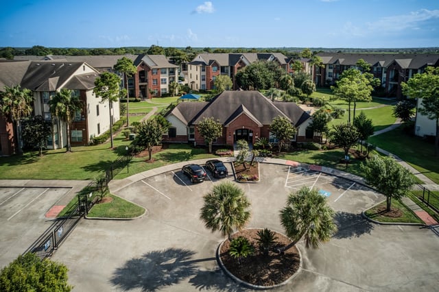 Aerial view of apartment complex buildings and central clubhouse with parking lot.