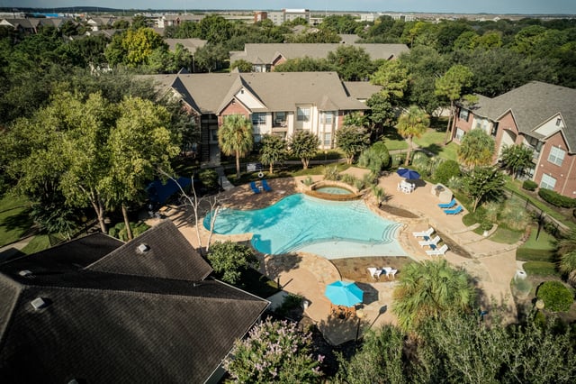 Aerial view of a resort-style swimming pool and hot tub area with lounge chairs and umbrellas.