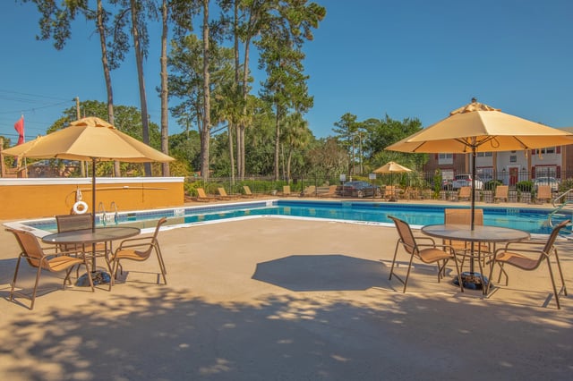 Outdoor swimming pool area with tables, chairs, and umbrellas.