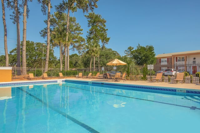 Large outdoor swimming pool with lounge chairs and tables under an umbrella.