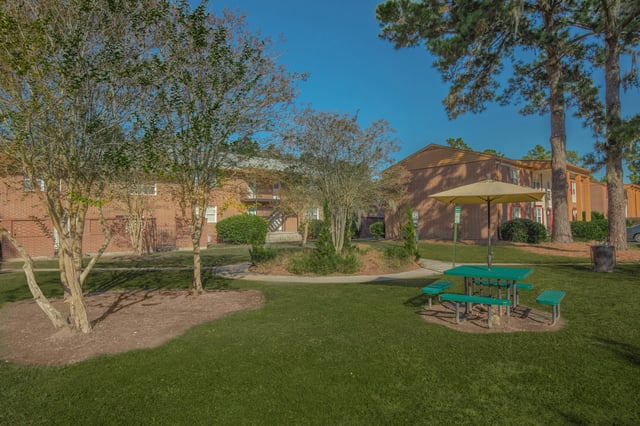 Picnic table with umbrella in grassy area with apartment buildings in background.