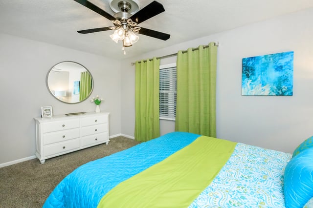 Bedroom with a dresser, mirror, and bed with blue and green bedding.