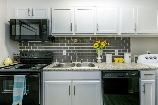 Modern kitchen with white cabinets, gray subway tile backsplash, black appliances, and granite countertops.
