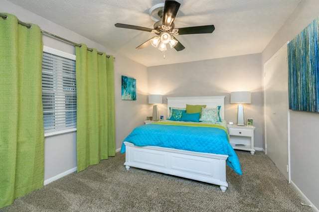 Bedroom with a queen-size bed, lime green curtains, and abstract art.