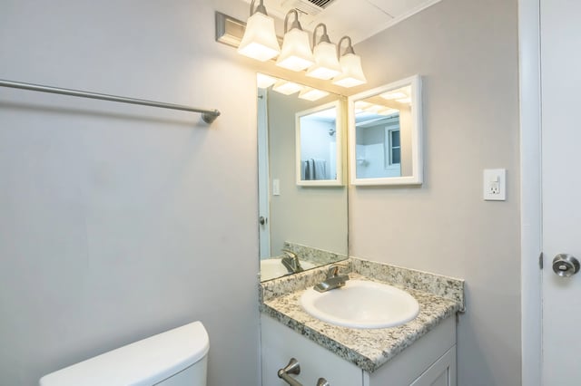 Modern bathroom vanity with granite countertop, white sink, and chrome faucet. Features a large mirror with a vanity light fixture above.