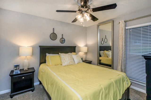 Queen-size bed with yellow bedding, nightstand, and floor-length mirror.