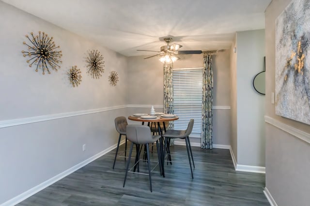 Modern dining area with a round table, four grey bar stools, and abstract wall art.