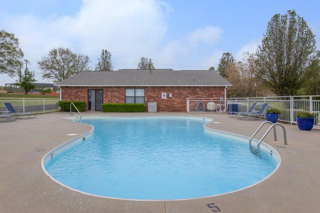 Sparkling outdoor swimming pool with lounge chairs and a brick building.