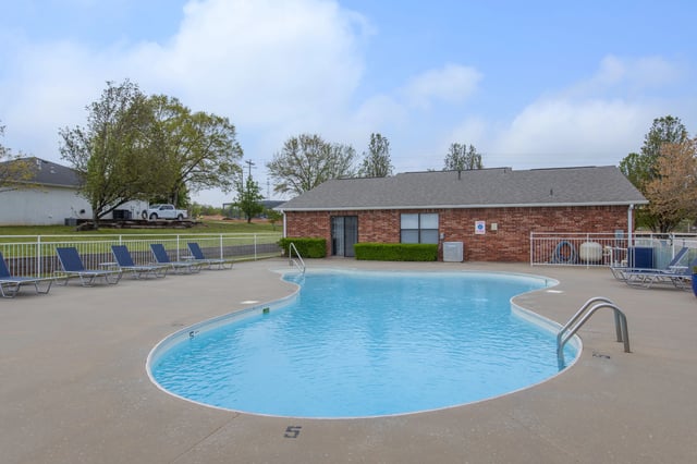 Outdoor swimming pool with lounge chairs and a brick building in the background.