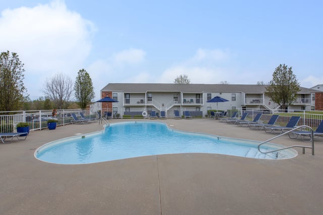 Resort-style swimming pool with lounge chairs and umbrellas in front of an apartment building.