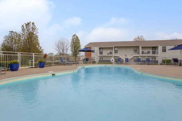 Outdoor swimming pool with lounge chairs and apartment building in background.