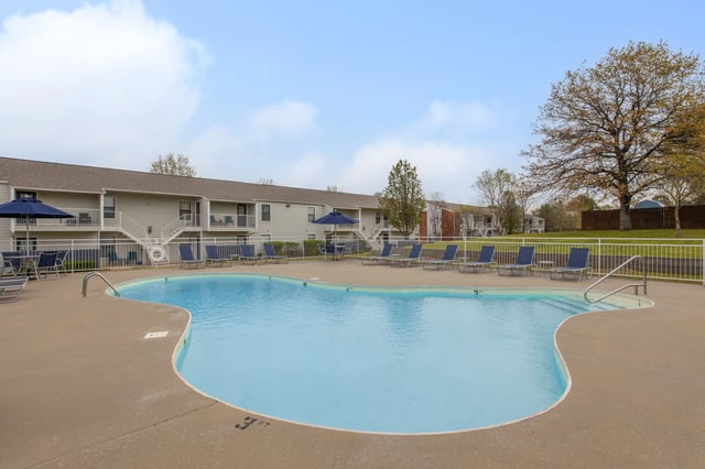Swimming pool with lounge chairs and umbrellas, apartment buildings in the background.