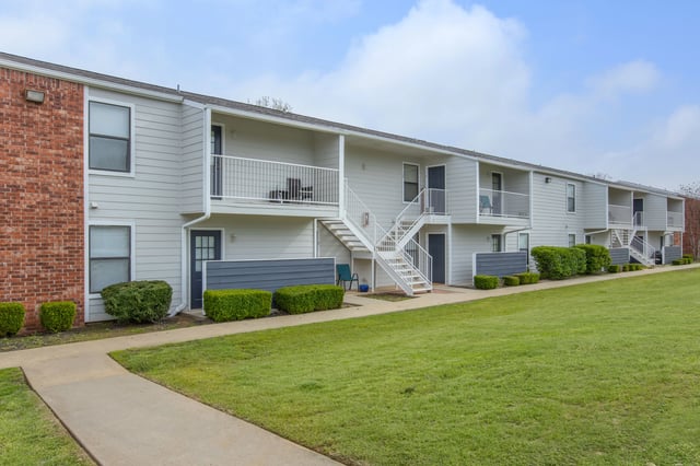 Exterior view of apartment buildings with balconies, stairs, and manicured lawns.