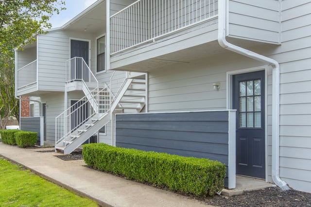 Exterior view of apartment building with stairs and green bushes.