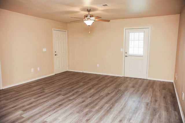 Empty living room with neutral walls, wood-look flooring, and a ceiling fan.