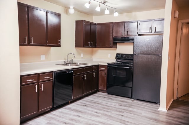 Kitchen with dark brown cabinets, white countertops, black appliances, and light wood laminate flooring.